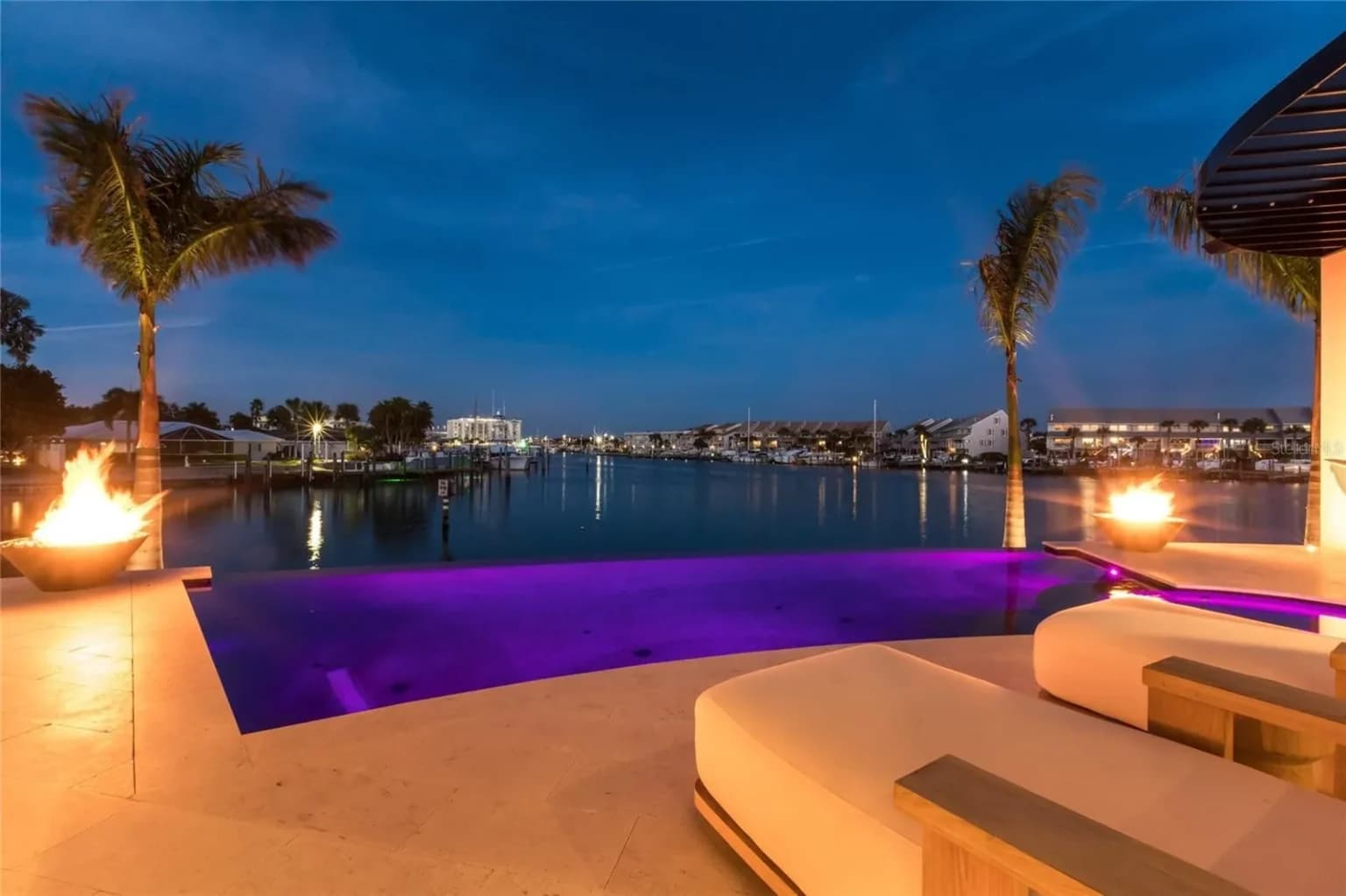 Pool lit purple at night with fire bowls, overlooking the bay